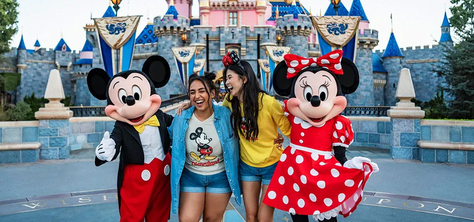 Visitors posing with Mickey and Minnie Mouse at Disneyland while wearing printed shirts.