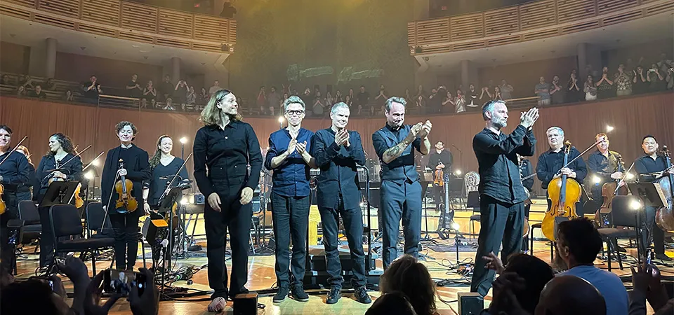 Orchestra bowing on stage in a Miami concert hall.